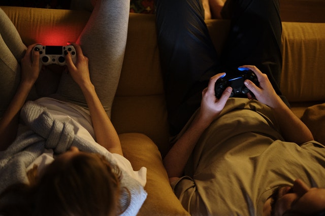 Kaksi ihmistä pelaa Playstationia sohvalla